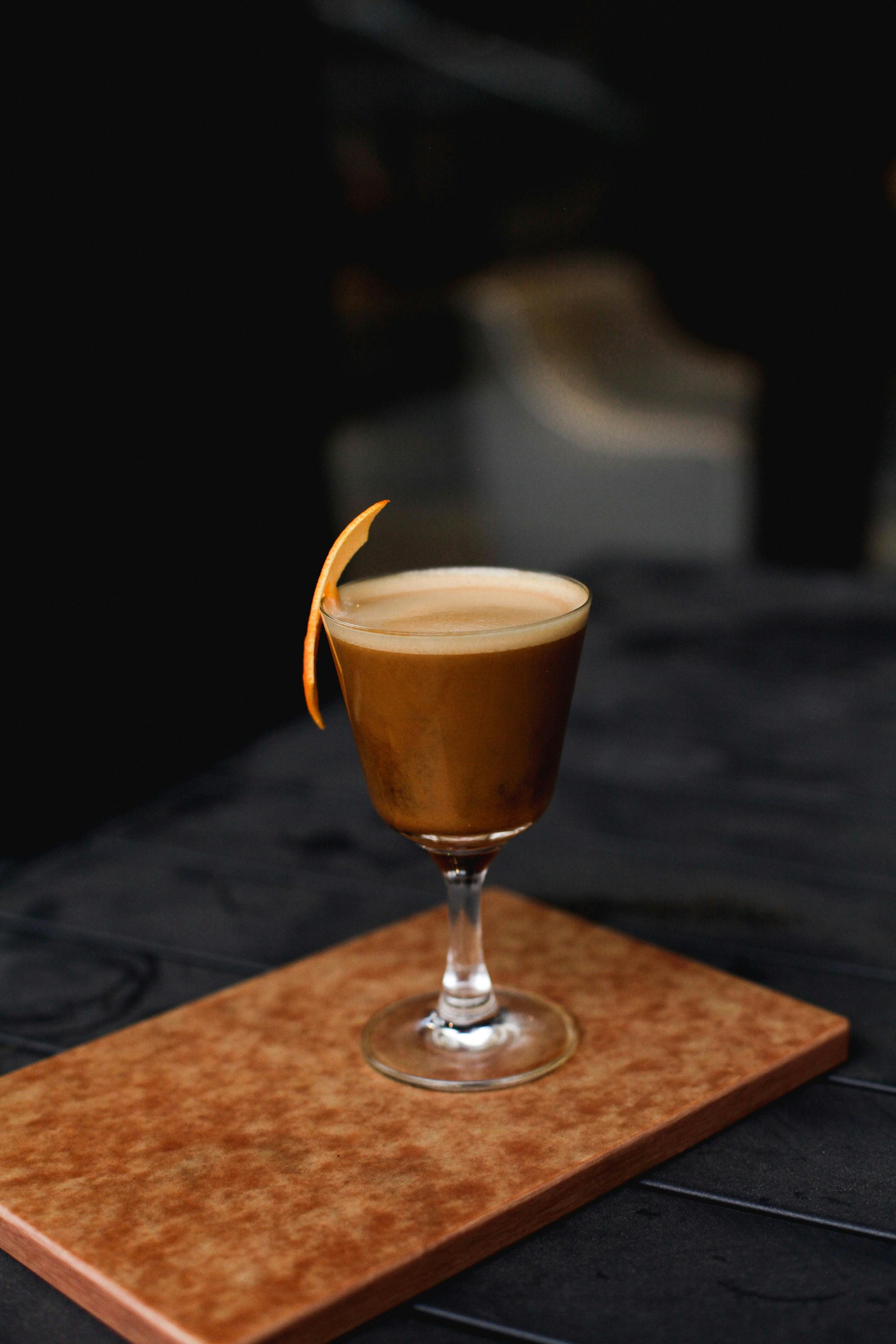 Espresso cocktail with an orange twist on a wooden board against a dark background