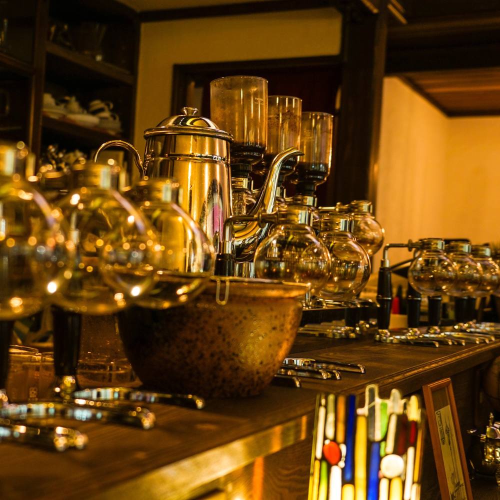 Collection of glassware and teapots on a wooden shelf with warm lighting, alchemist scene