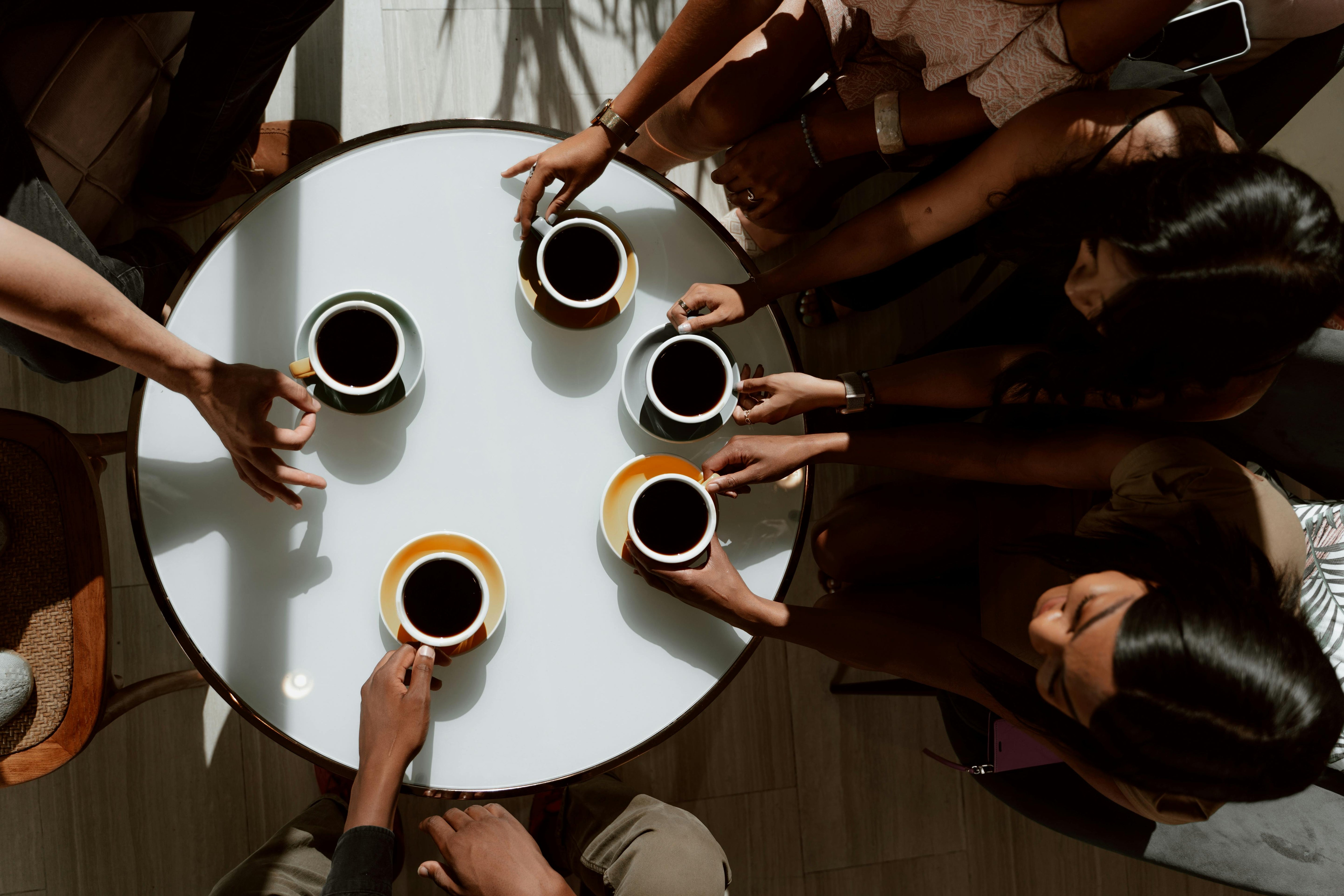 People sitting around a round table with coffee cups reaching out to drink