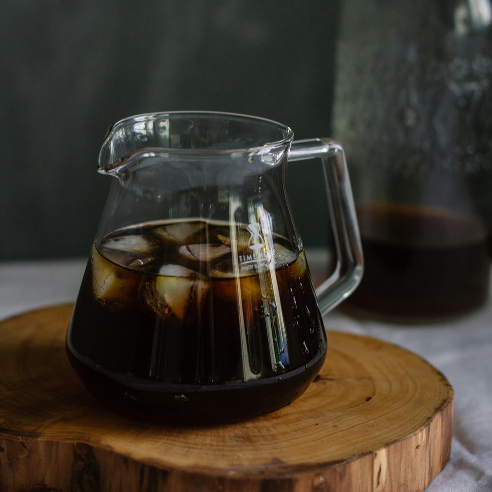 Clear glass pitcher with iced coffee on a wooden surface