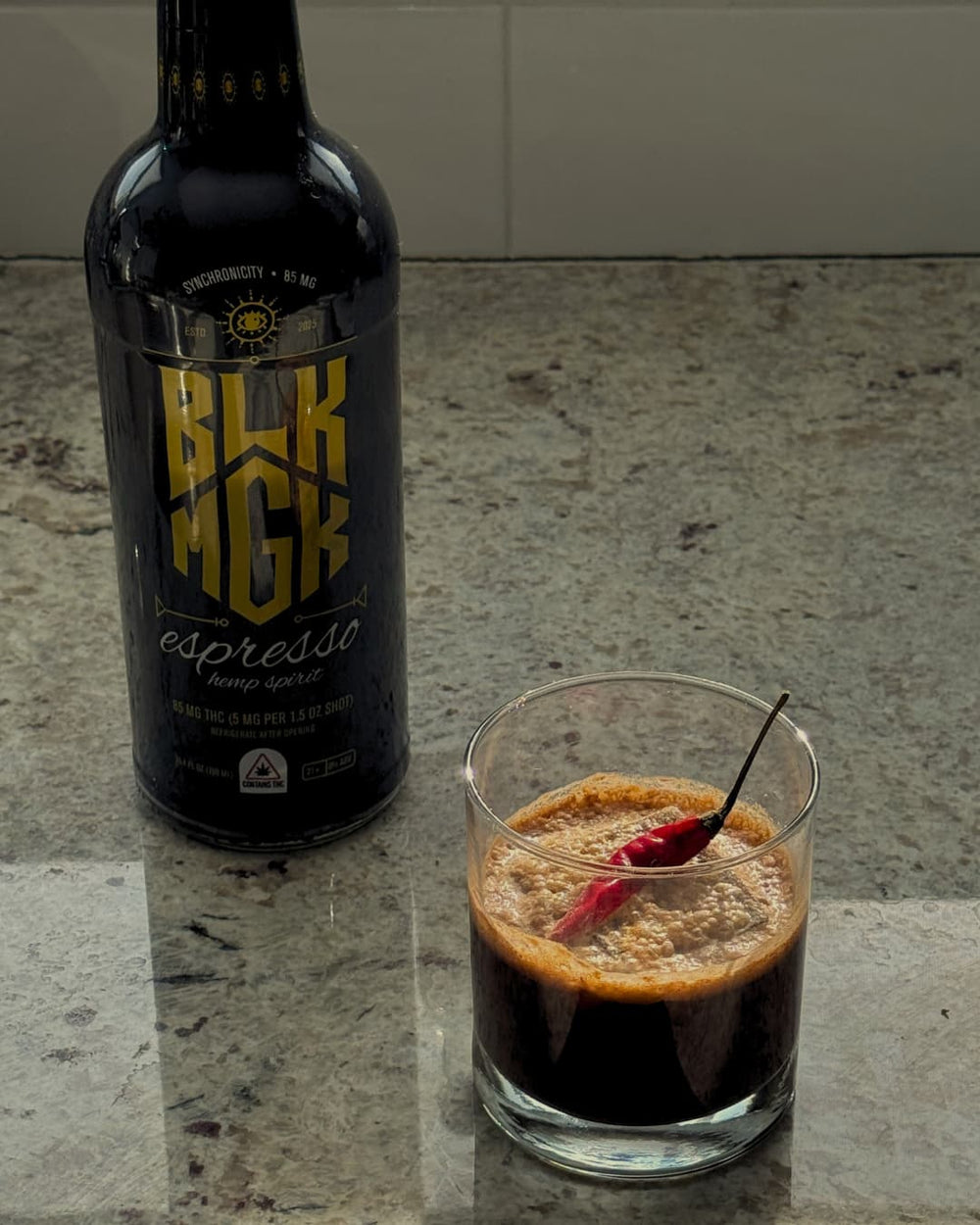 Chili chocolate espresso cocktail with hot chili pepper on top and bottle of BLK MGK to the left