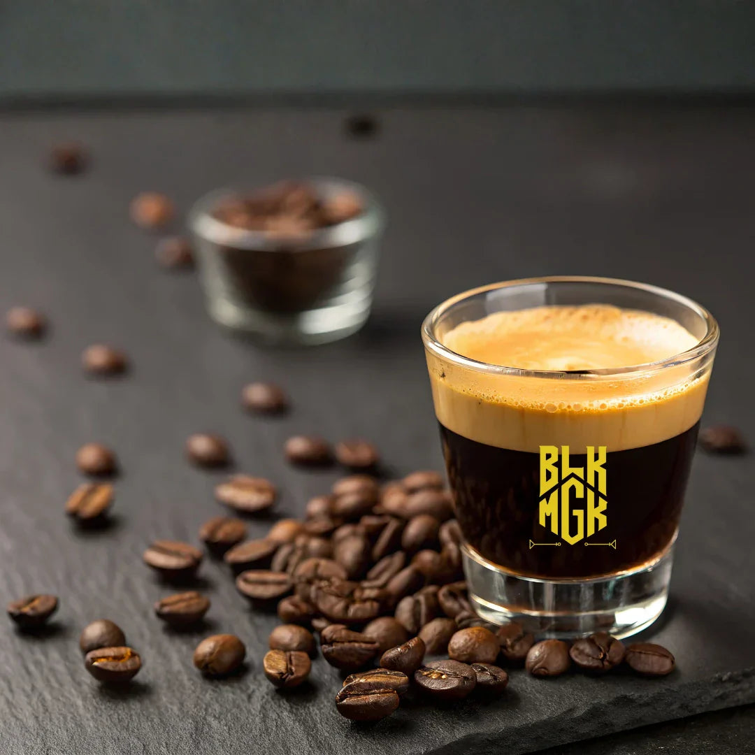 Shot of BLK MGK espresso hemp spirit surrounded by coffee beans with yellow logo on shot glass
