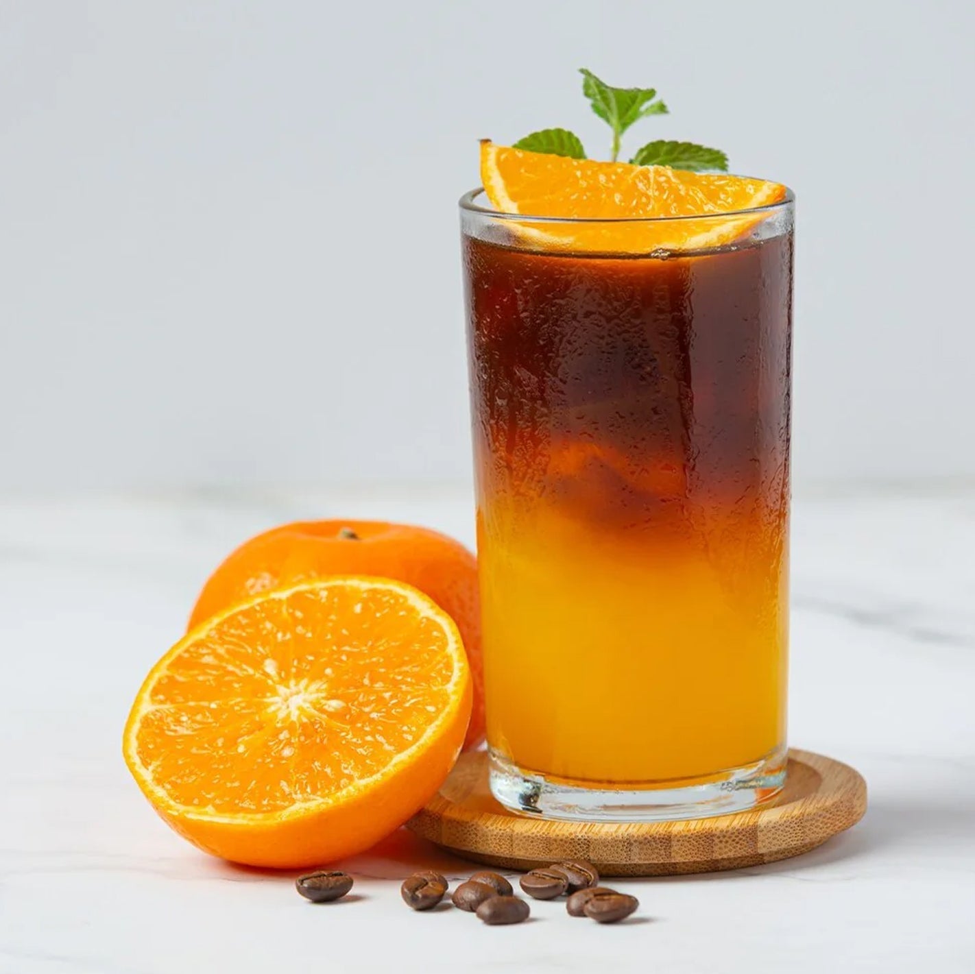 citrus sigil cocktail in highball glass with orange juice at bottom and BLK MGK espresso hemp spirit at top, garnished with orange slice and mint sprig on wooden coaster 