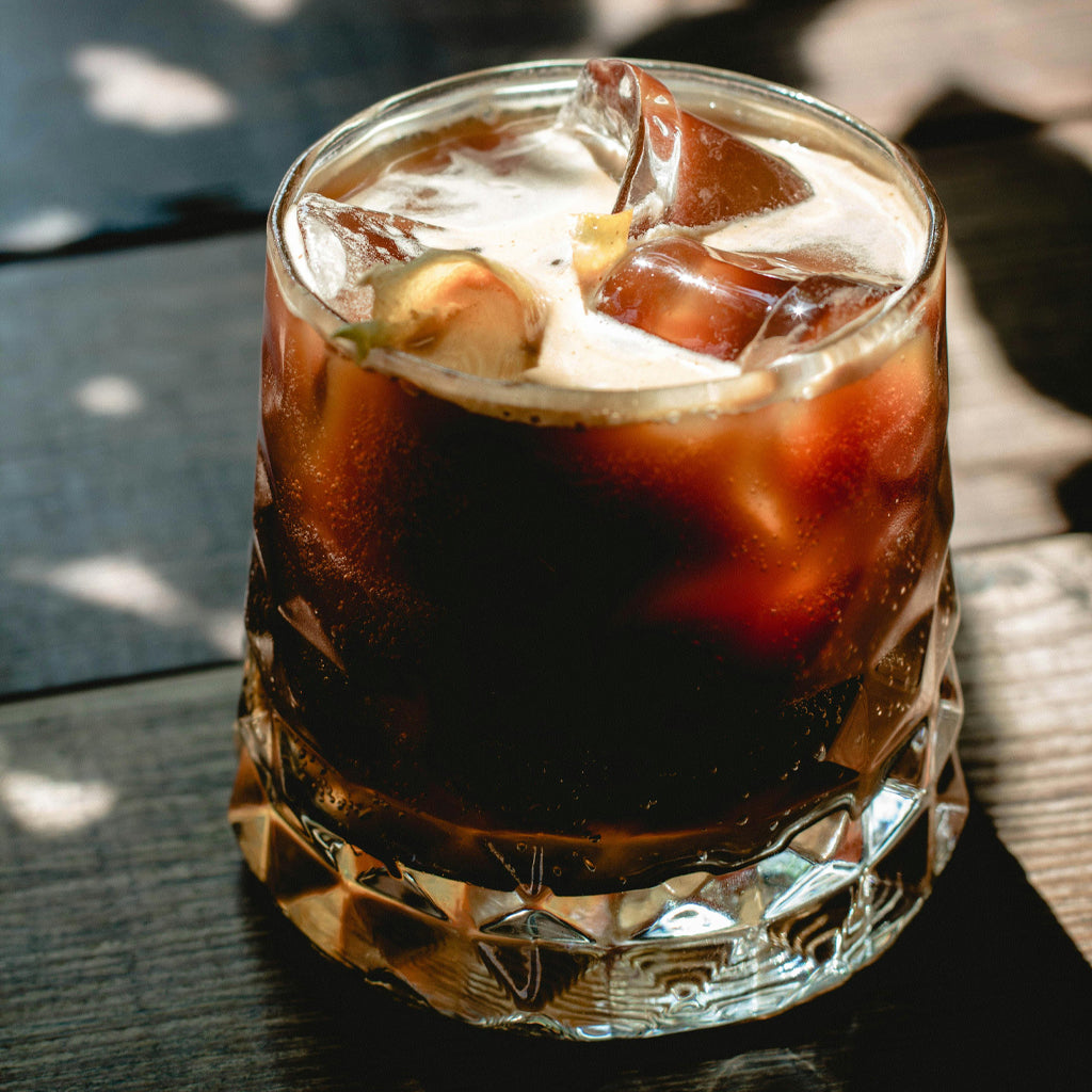 Glass of iced coffee with ice cubes on a wooden surface and shadowy lighting