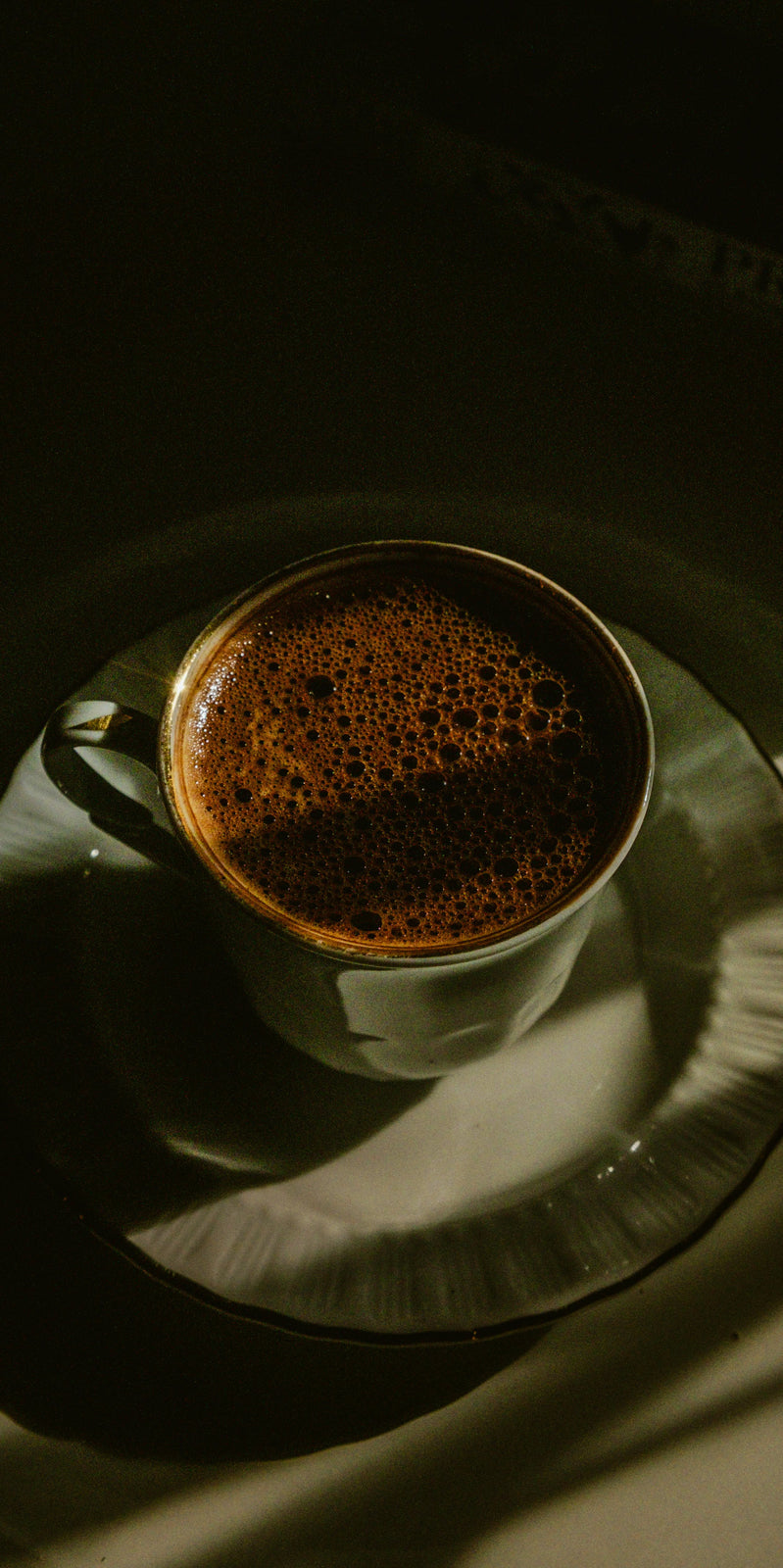 Cup of fresh coffee on a dark surface with a soft focus and green hues