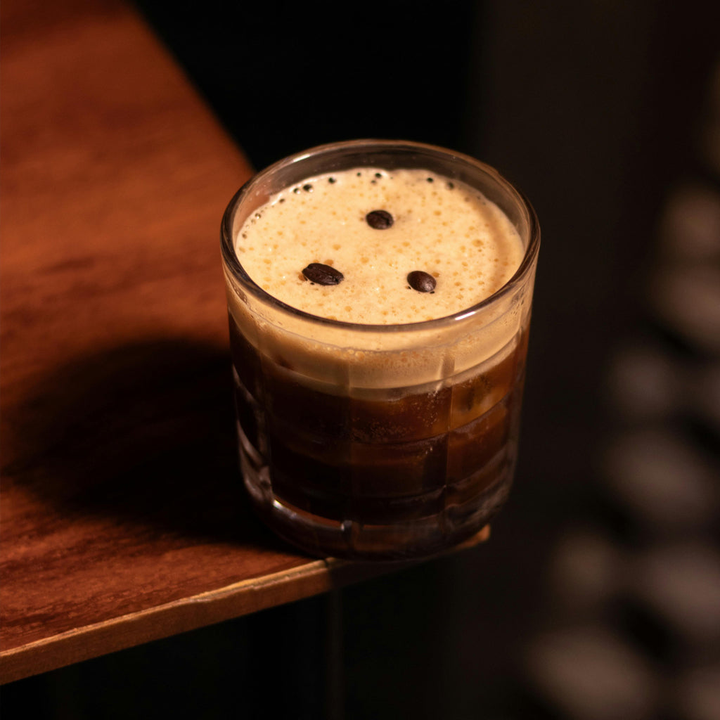 Lowball glass of espresso martini with a creamy top on corner of wooden table